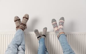 drei Paar Beine kreuzen sich vor einer Heizung; alle tragen warme Socken