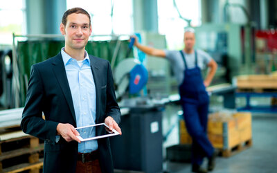 Person im Anzug steht mit Tablet in einem Industrie-Gebäude